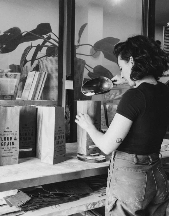 A baker scooping fresh flour into Almanac paper bags.