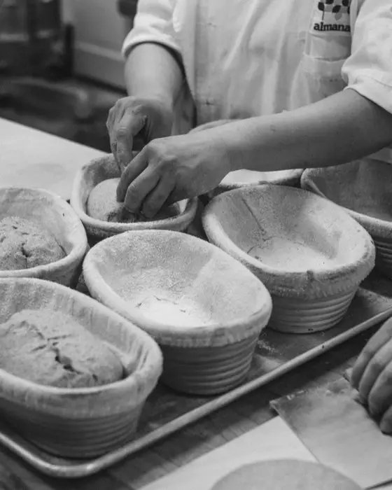 Hands shaping dough on a floured bench.